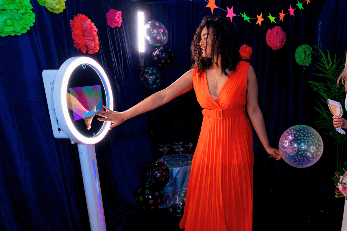 Guest using an interactive selfie photo booth with ring light at a colorful party decorated with balloons and festive decorations.
