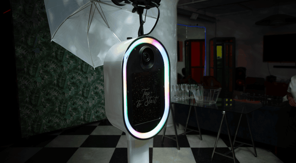 Modern selfie photo booth with LED ring light and studio umbrella lighting set up at an indoor event venue.